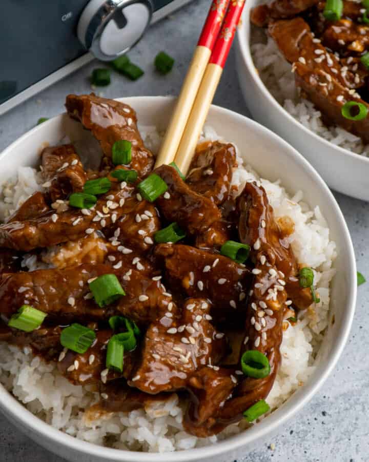 Close up of slow cooker teriyaki beef over white rice with chopsticks in it.