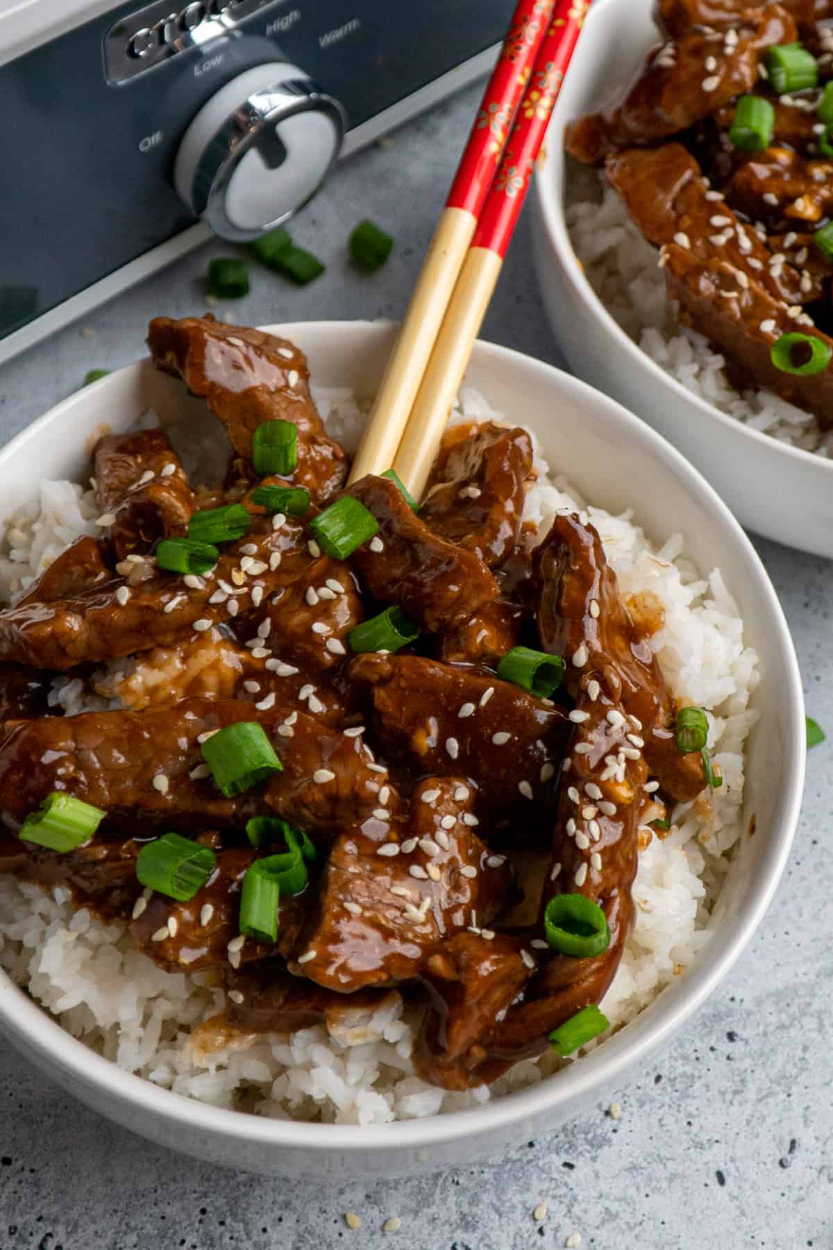 Close up of slow cooker teriyaki beef over white rice with chopsticks in it.