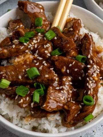 Slow cooker teriyaki beef over white rice with chopsticks in it.