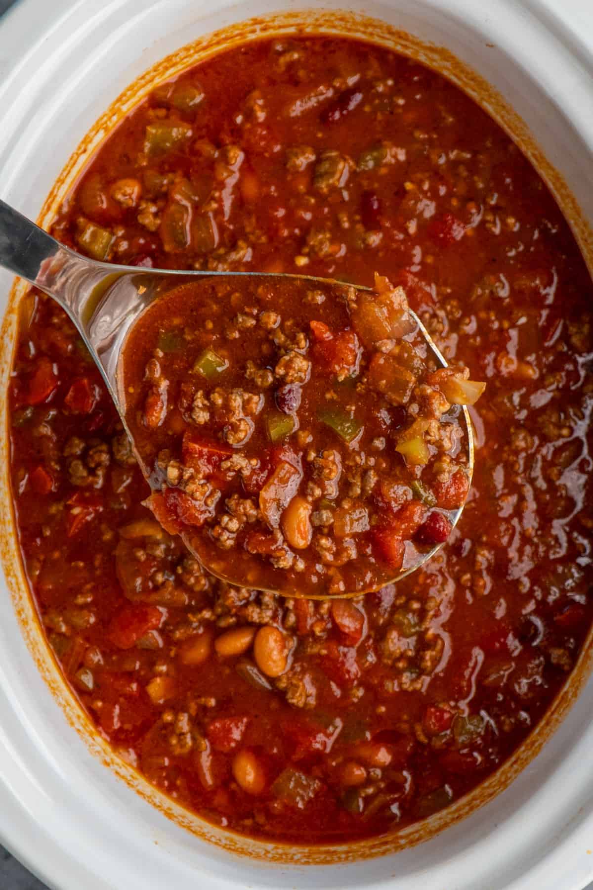 The best chili in a ladle over a slow cooker full of chili.