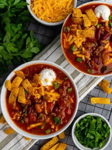 Two bowls of the best Crock Pot chili topped with cheese, fritos, sour cream and green onions.