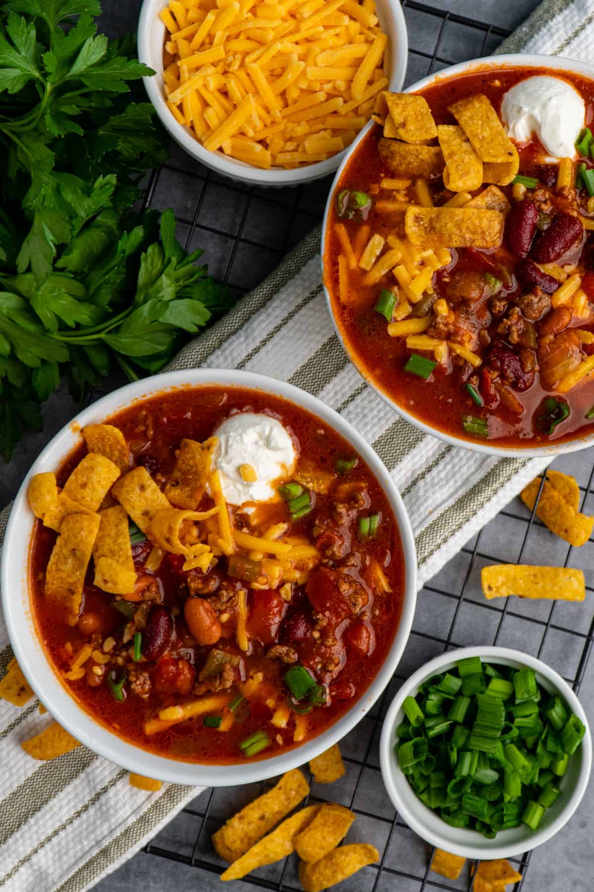 Two bowls of the best Crock Pot chili topped with cheese, fritos, sour cream and green onions.