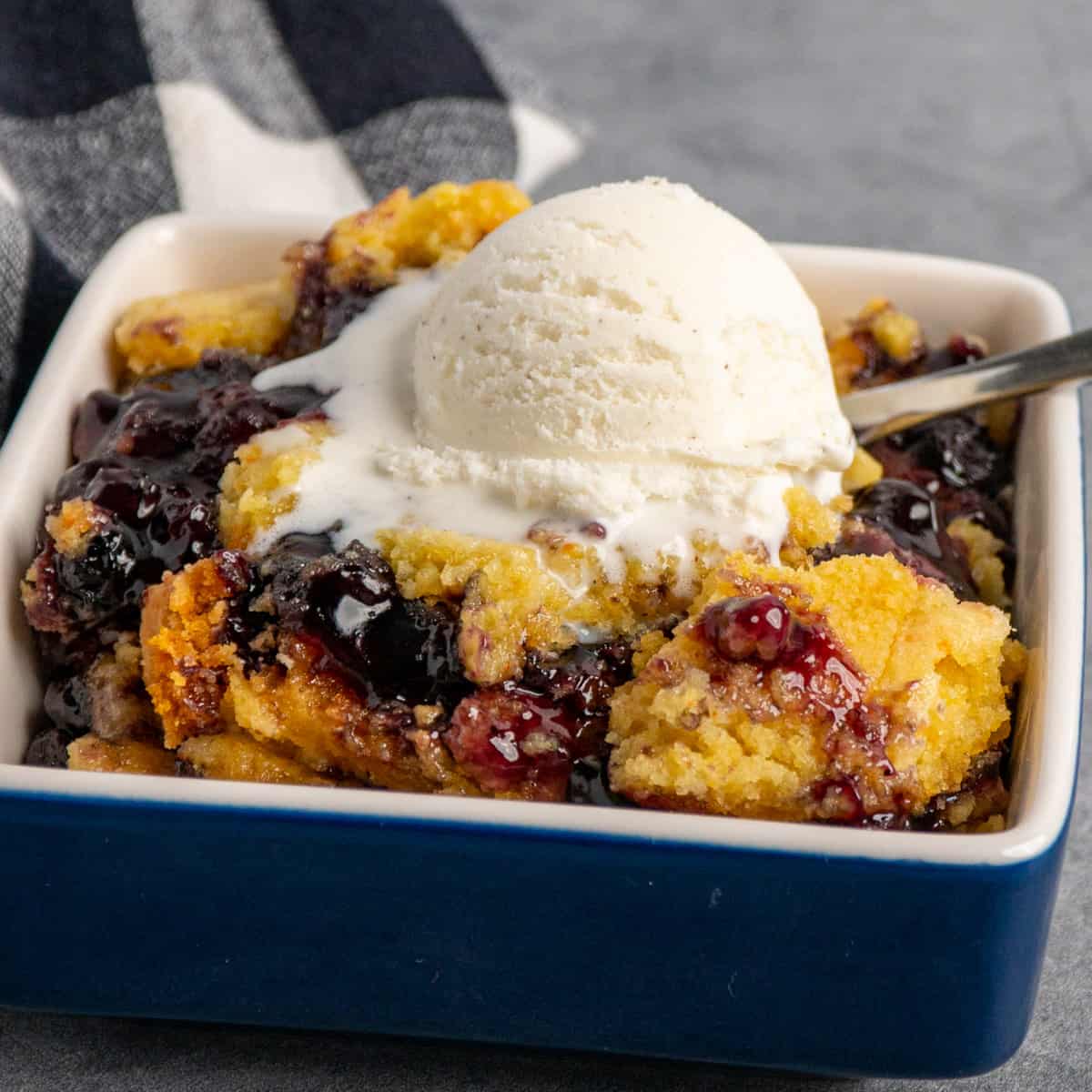 Close up of crock pot blueberry cobbler in a blue bowl with ice cream