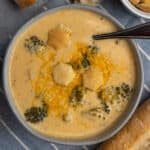 Overhead look at crock pot broccoli cheese soup in a gray bowl with cheese on top.