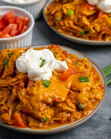Two plates of crock pot chicken enchilada casserole with sour cream on top.