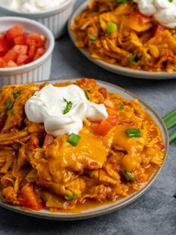 Two plates of crock pot chicken enchilada casserole with sour cream on top.