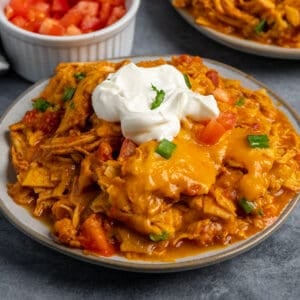 A plate of crock pot chicken enchilada casserole with sour cream on top.