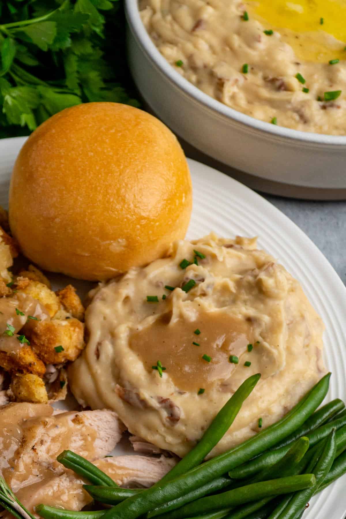 Garlic red mashed potatoes and gravy on a white plate with stuffing, turkey, green beans and a roll.