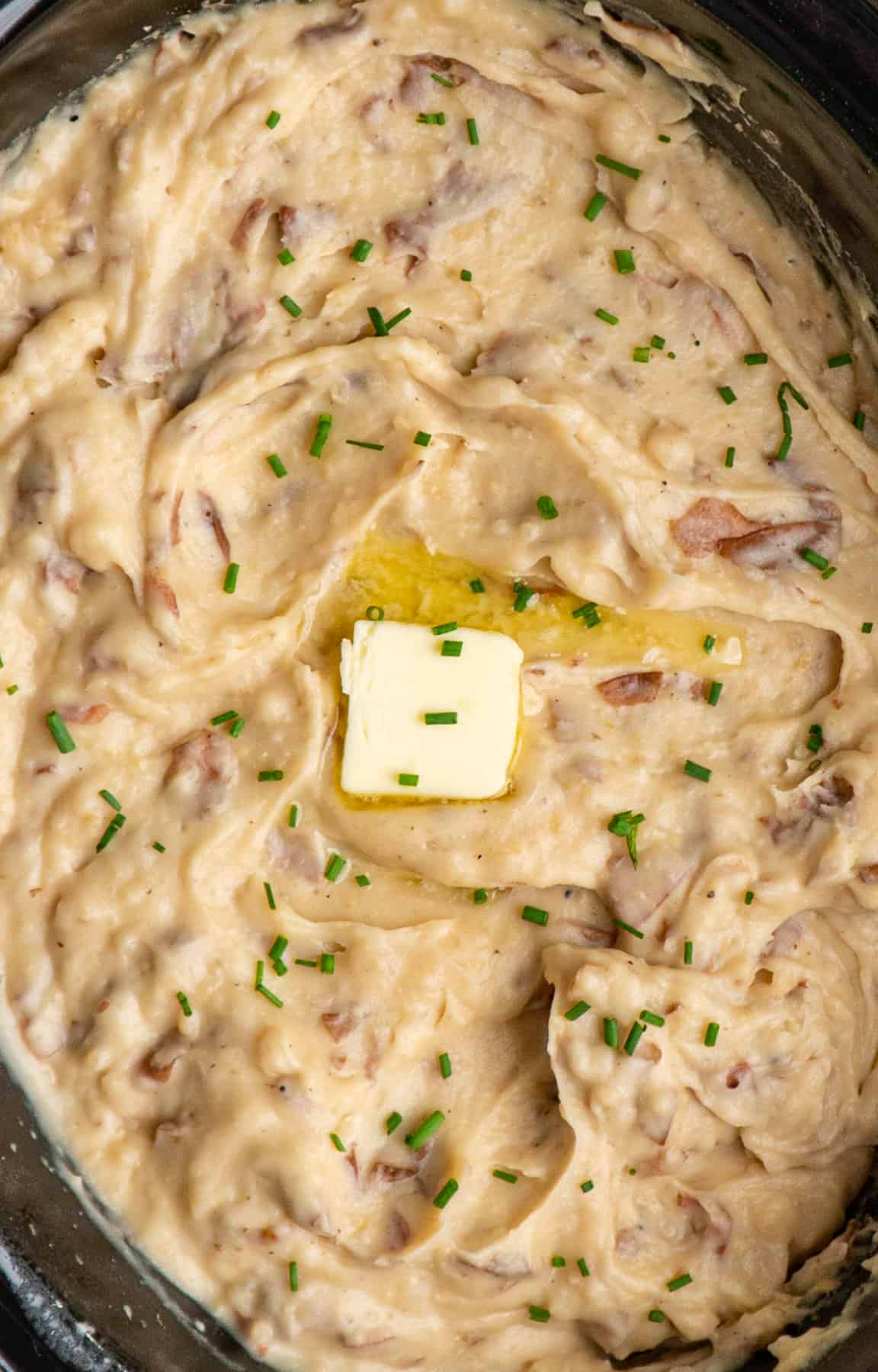 Overhead look at Crock Pot garlic mashed potatoes with chives and butter on top.