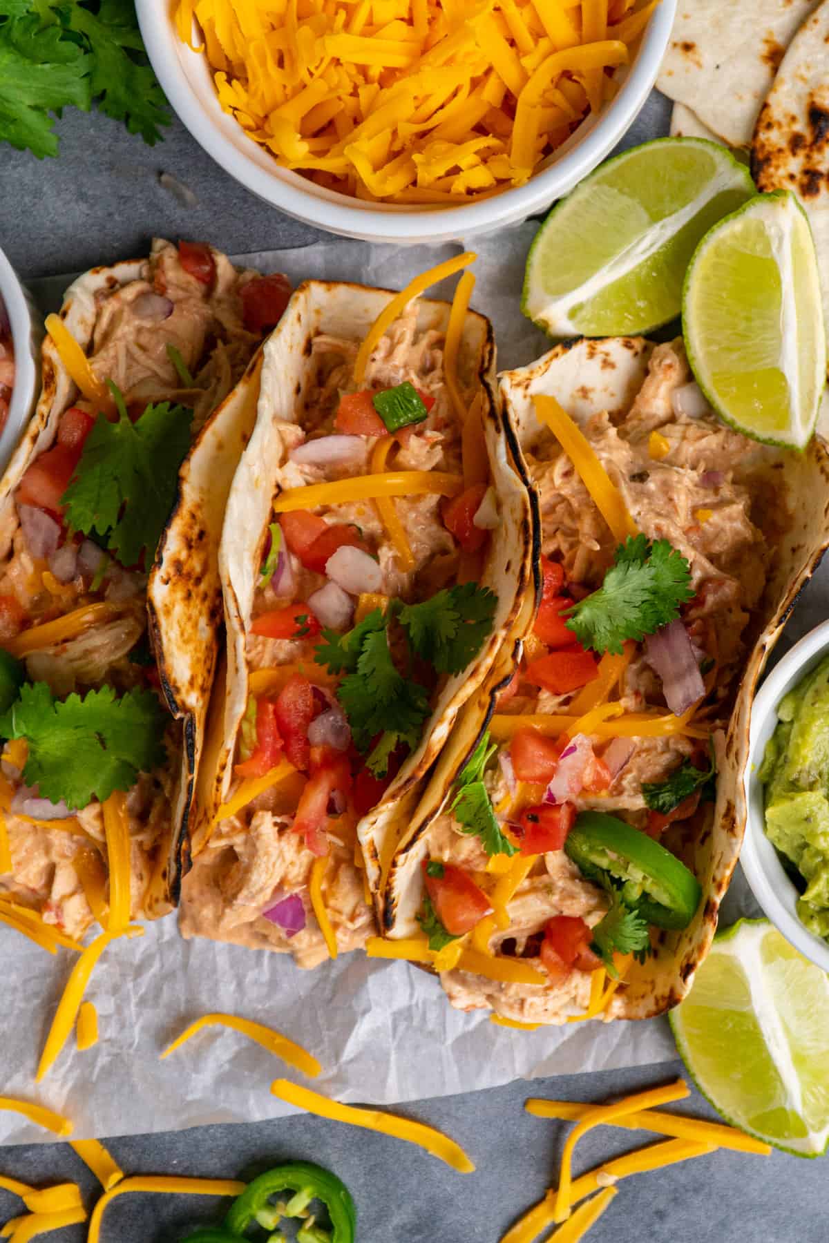 Three chicken tacos with toppings and limes in the background.