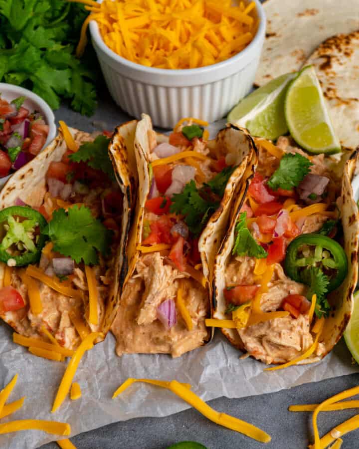 Image of three creamy crock pot salsa chicken tacos on a piece of parchment paper.