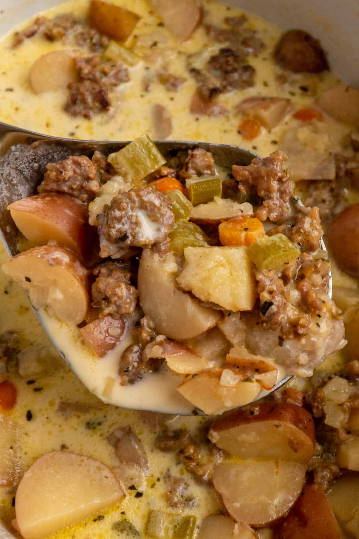 Close up of sausage and potato soup in a laddle over a slow cooker.