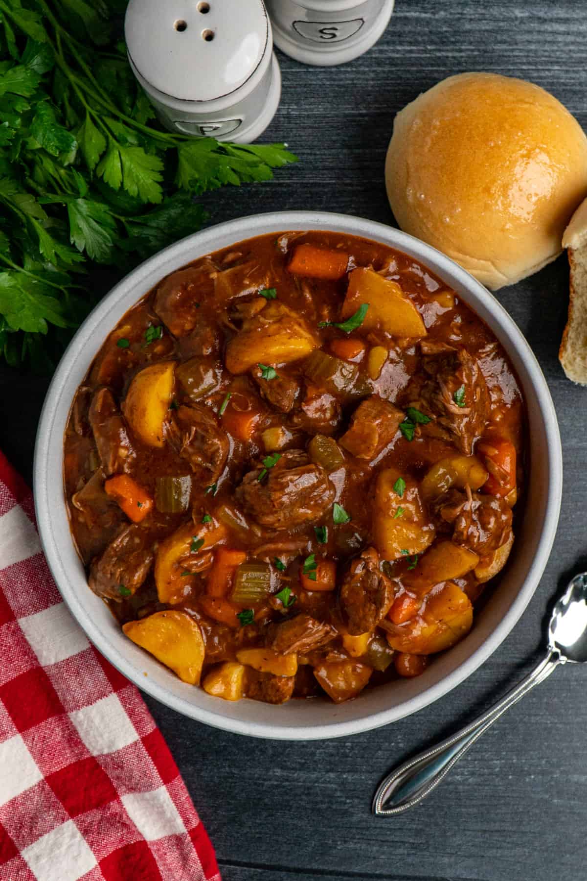 Overhead look at slow cooker beef stew in a white bowl with parsley and a roll in the background