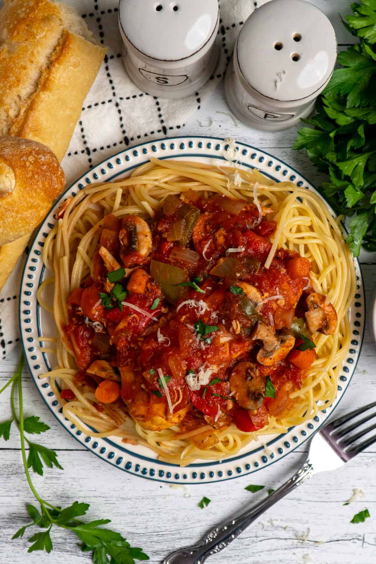 Overhead look at slow cooker chicken cacciatore on a plate of pasta and side of bread.