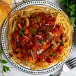 Overhead look at slow cooker chicken cacciatore on a plate of pasta and side of bread.