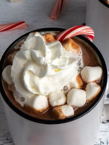 Slow cooker hot chocolate in a white mug with marshmallows, candy cane and whip cream on top