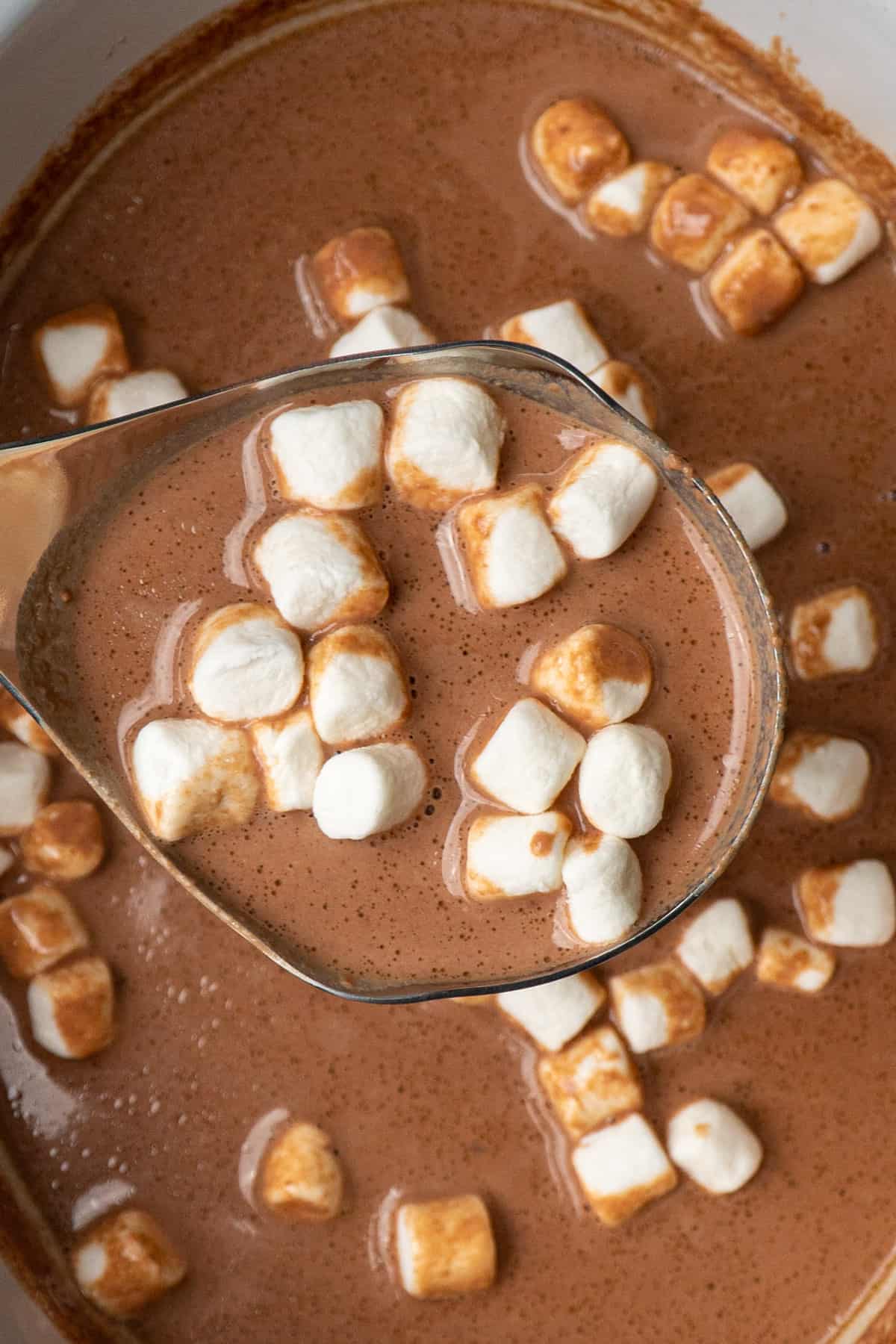 Hot chocolate in a ladle over a crock pot with marshmallows in it