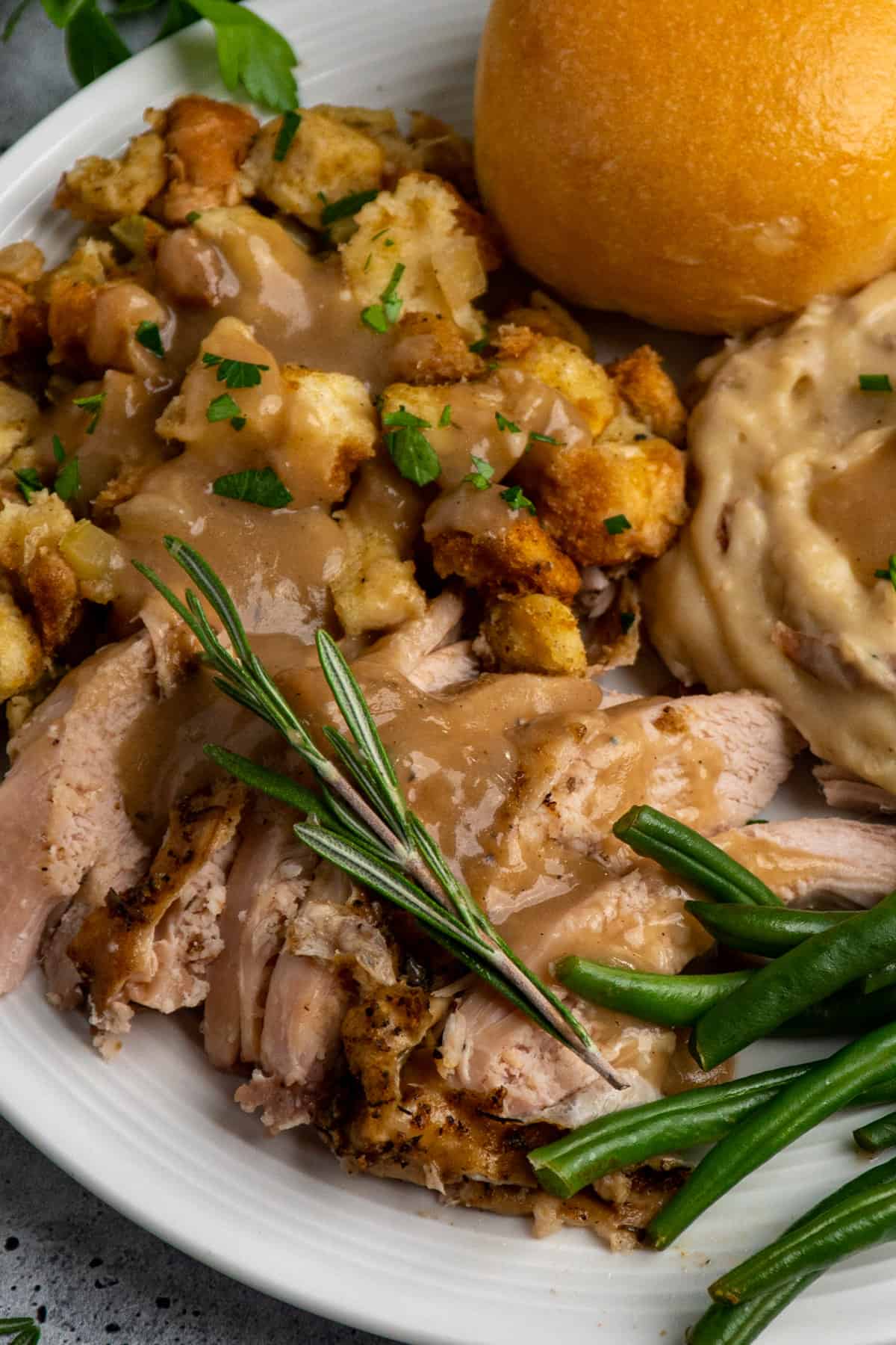 Slow cooker turkey breast on a white plate with stuffing and mashed potatoes.