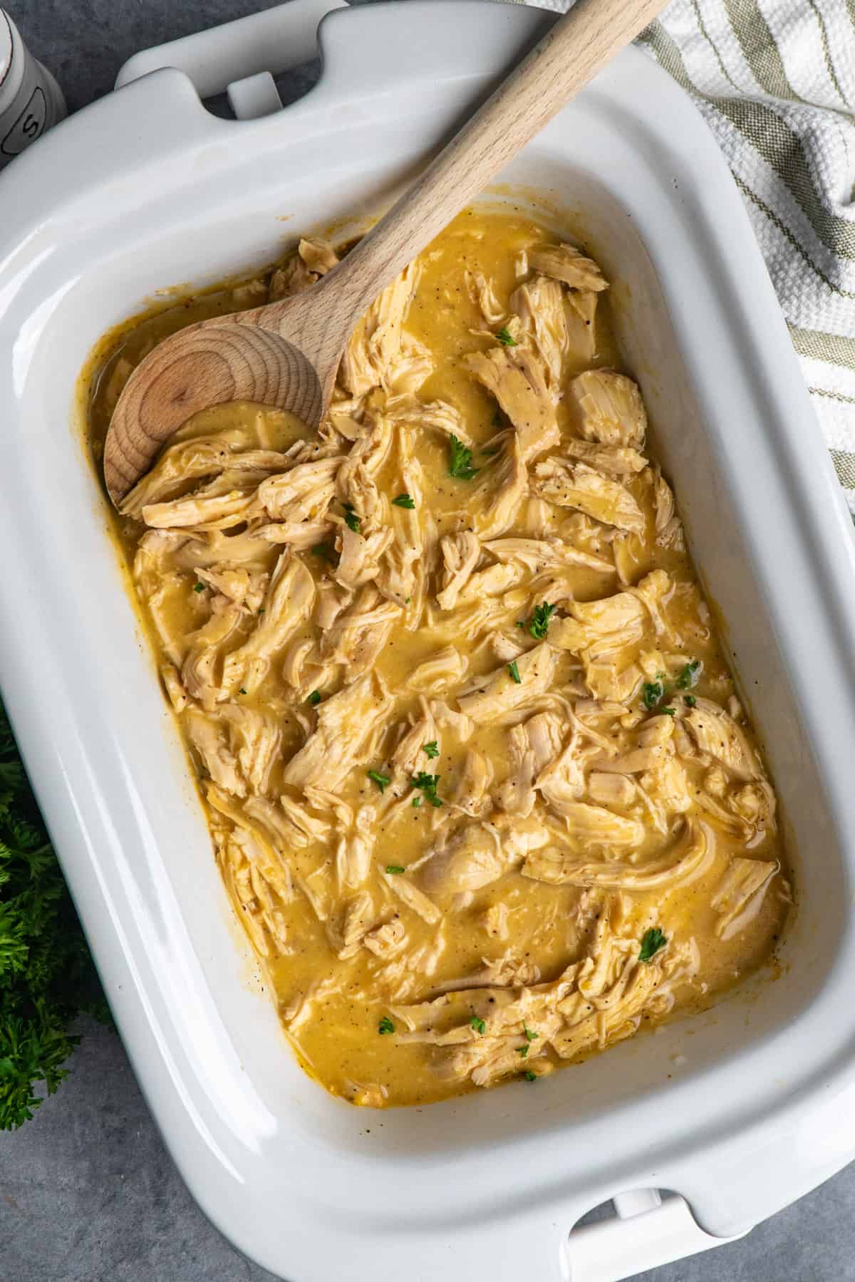 Chicken and gravy in a slow cooker with a wooden spoon.
