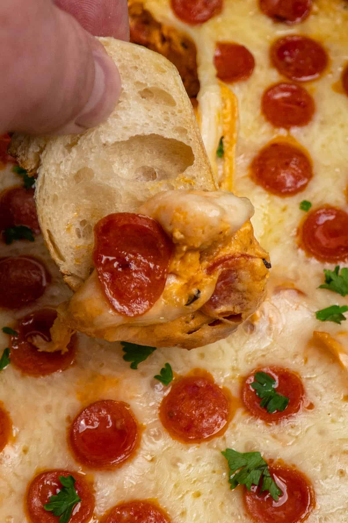 A piece of bread being dipped into crock pot pizza dip