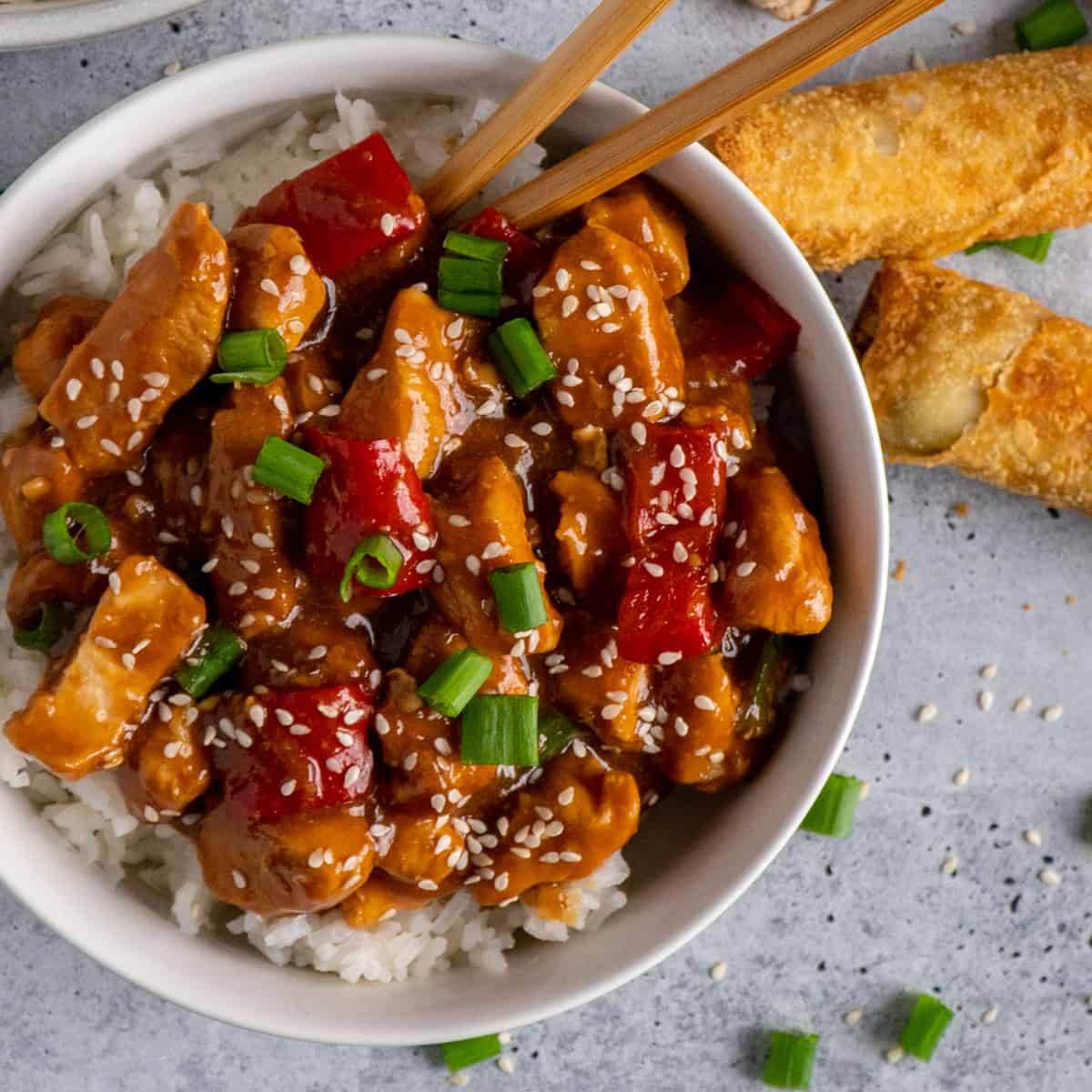 Sesame chicken over a bowl of rice garnished with green onions