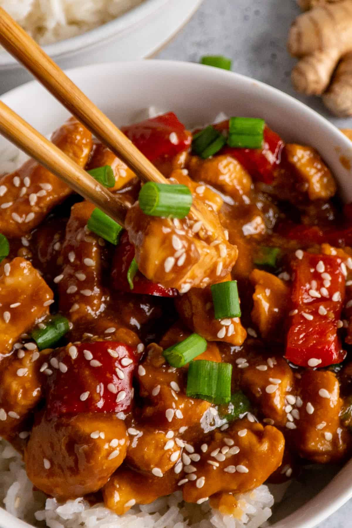 Chopsticks holding a piece of sesame chicken garnished with green onion.
