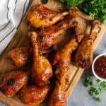 Crockpot BBQ chicken legs on a wood cutting board garnished with chopped parsley.