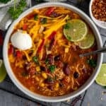 Over head look at slow cooker chicken taco soup in a bowl garnished with cheese, sour cream and limes.