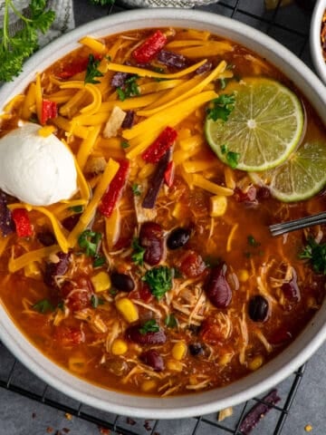 Over head look at slow cooker chicken taco soup in a bowl garnished with cheese, sour cream and limes.