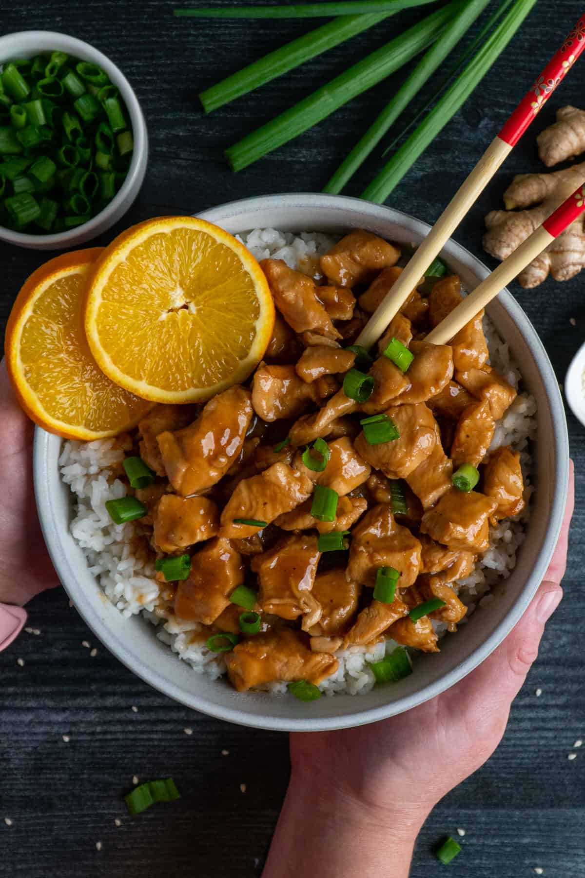 Two hands holding Crock Pot orange chicken over a bowl of rice