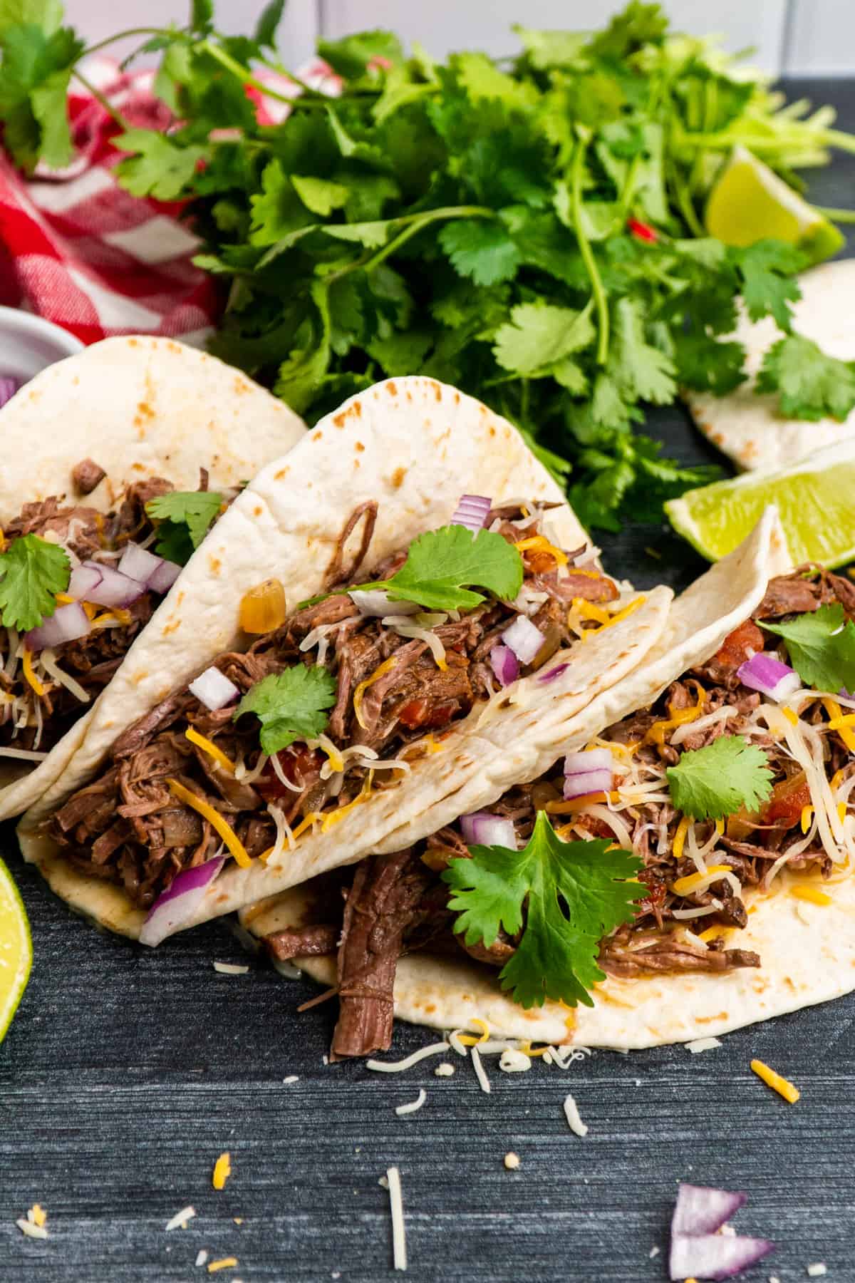 Crock Pot shredded beef tacos in flour tortillas and garnished with onions and cilantro.
