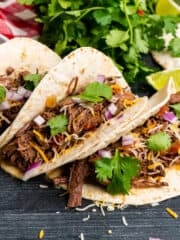 Slow cooker shredded beef tacos in flour tortillas and garnished with onions and cilantro.