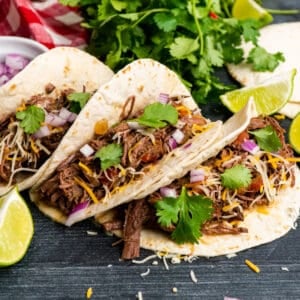 Slow cooker shredded beef tacos in flour tortillas and garnished with onions and cilantro.