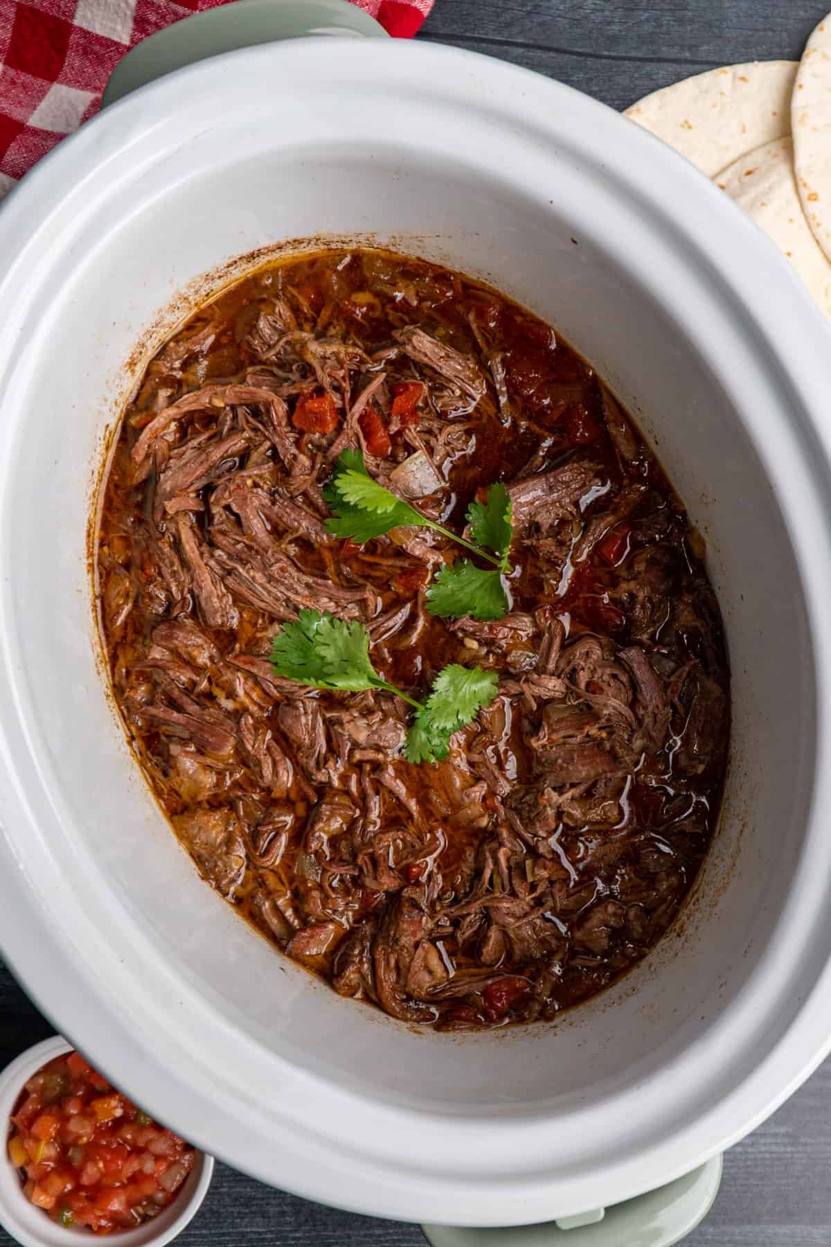 Shredded beef in a white crock pot garnished with cilantro.