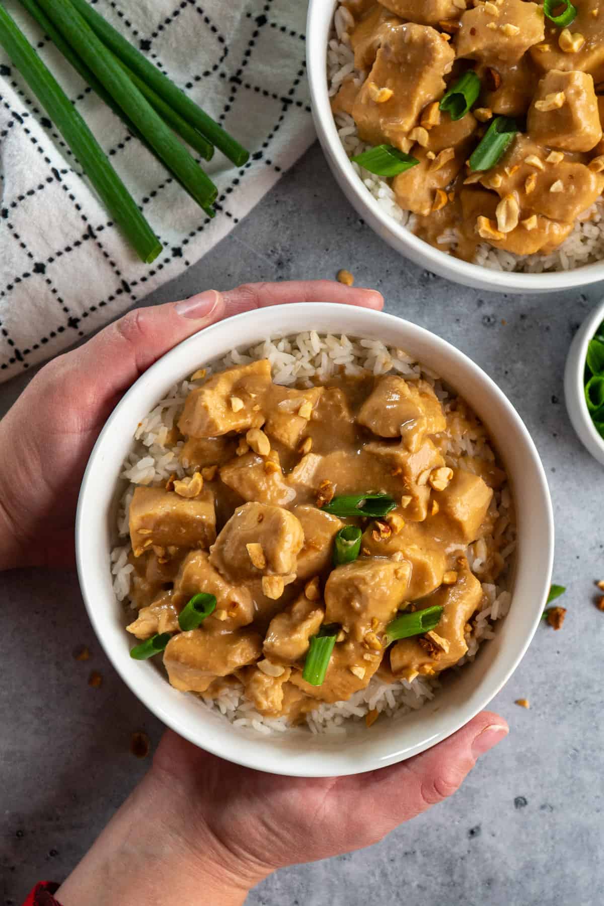 Thai peanut chicken in a bowl of rice with hands holding it.