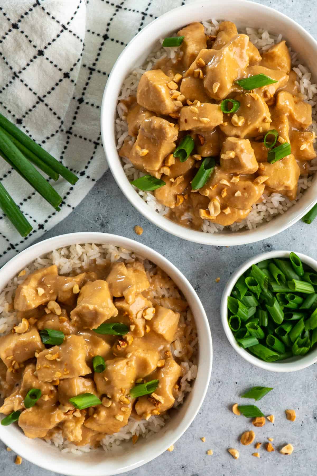 Thai peanut chicken in two bowls over rice garnished with peanuts and green onions.