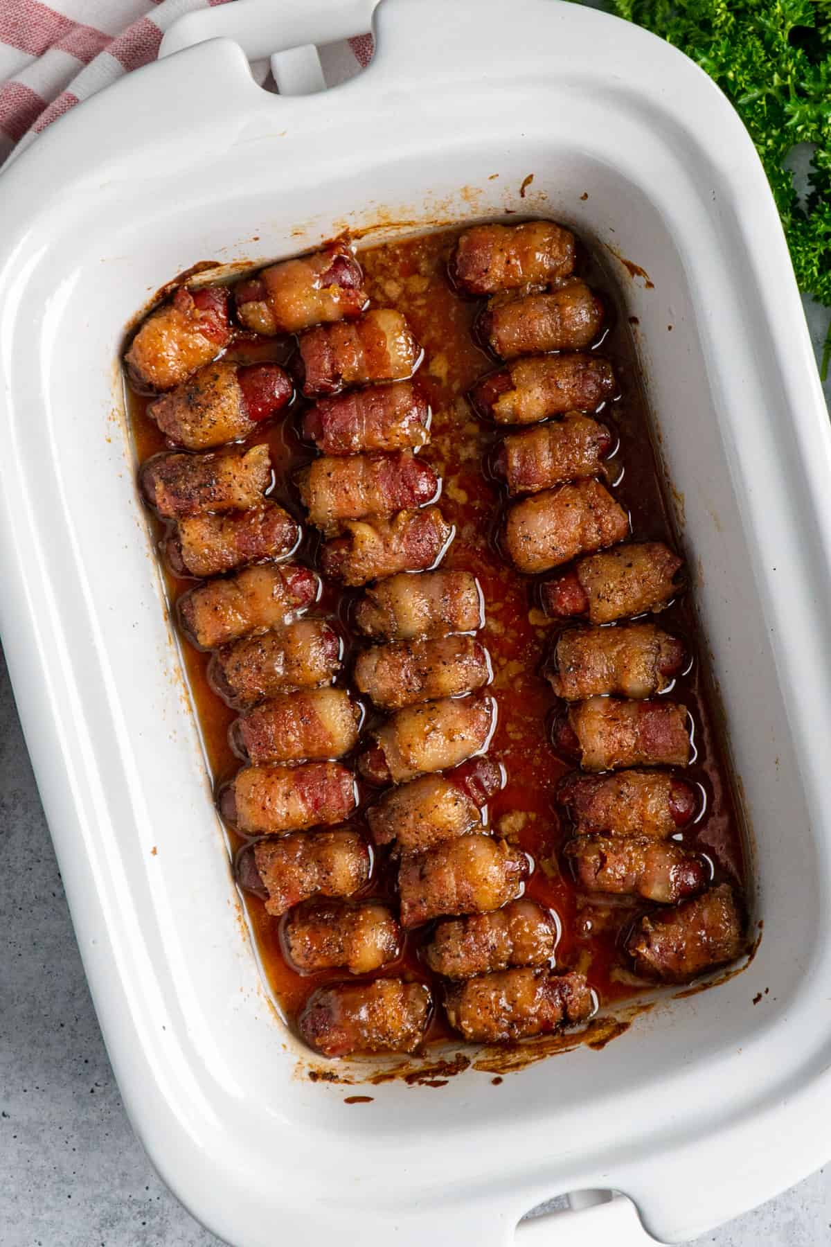 Bacon wrapped sausages in a white crock pot.