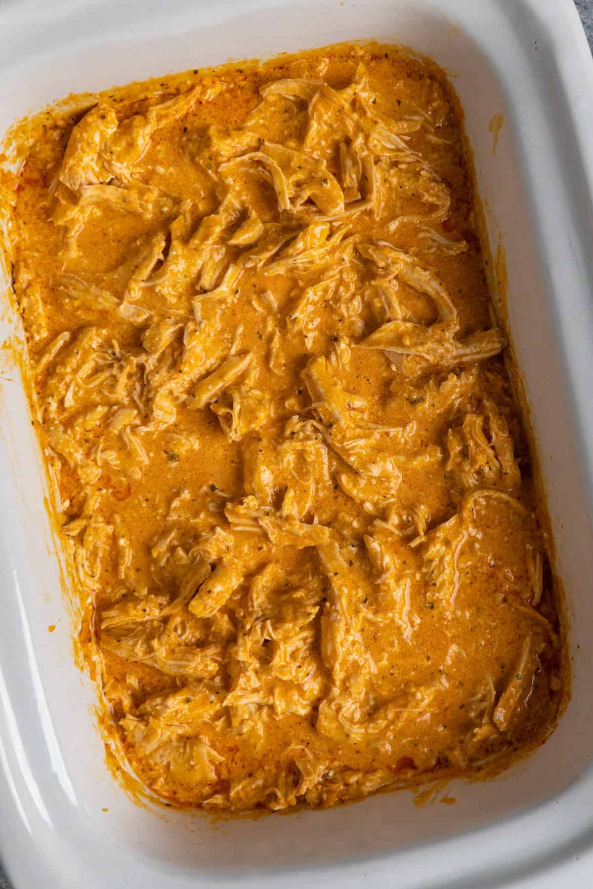 Buffalo chicken in a white slow cooker.