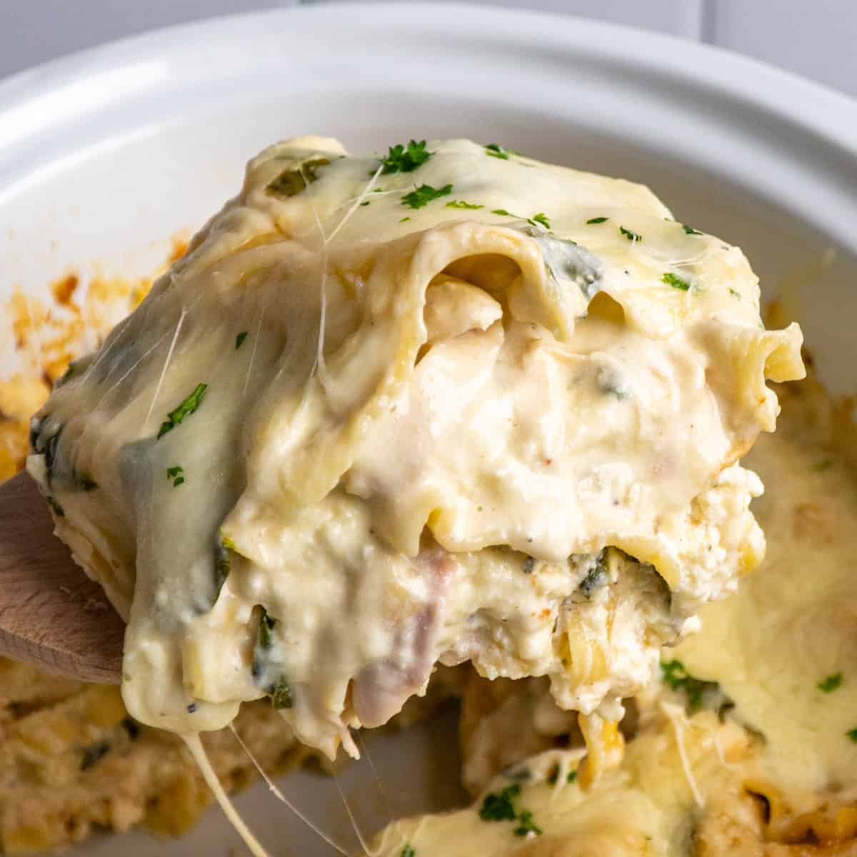 A spoon holdin up a piece of crock pot chicken lasagna