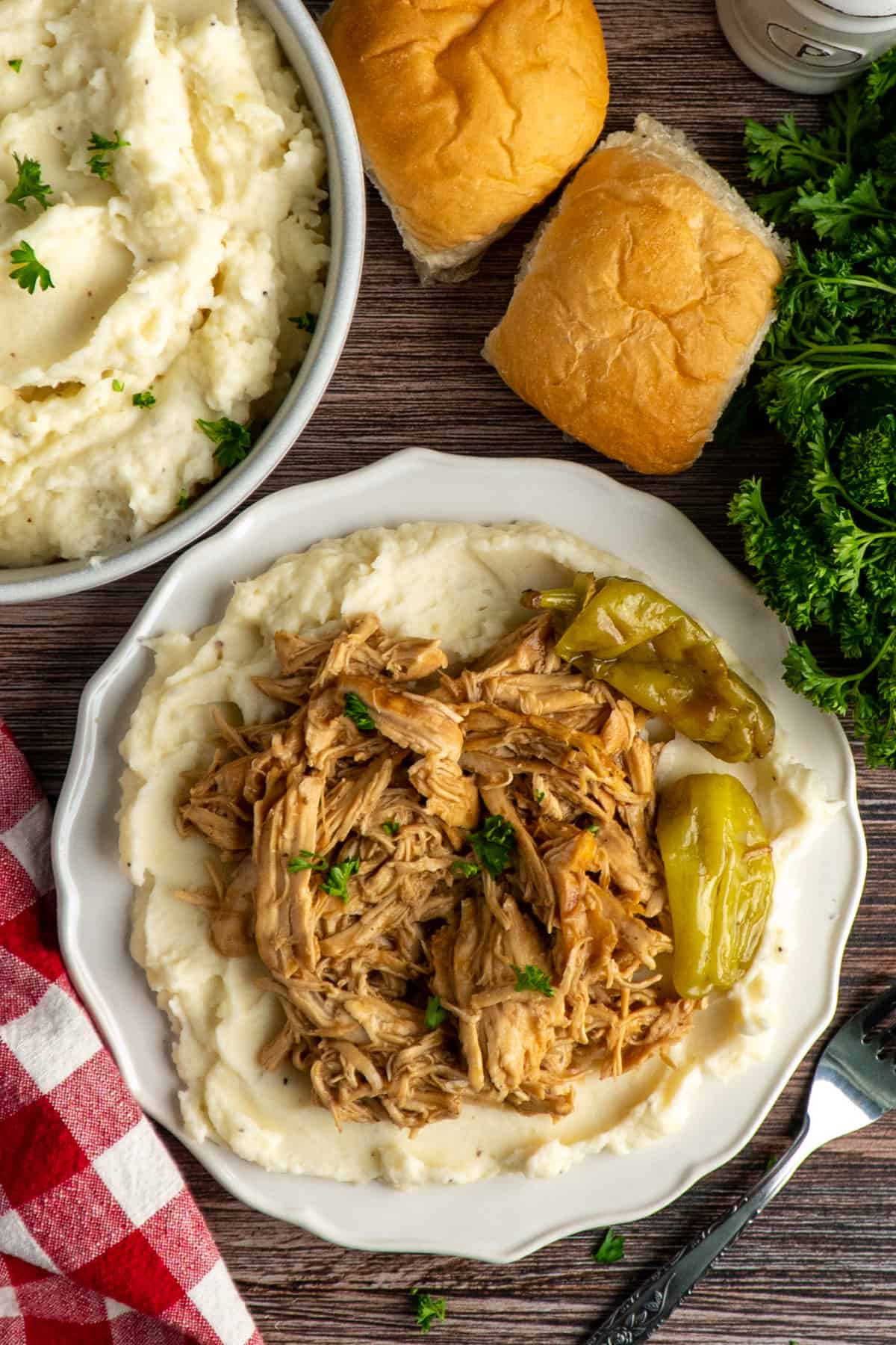 Shredded chicken on a plate of mashed potatoes garnished with pepperoncini peppers.