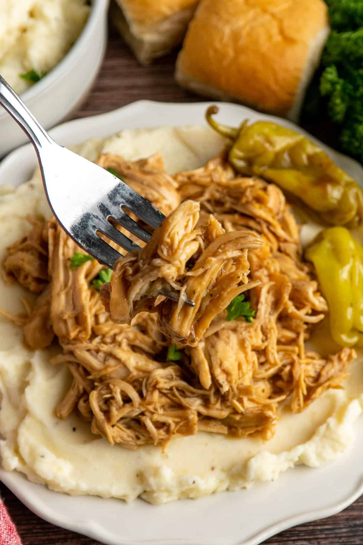 Mississippi chicken in a crock pot served on a plate with a bite on a fork up over the plate.