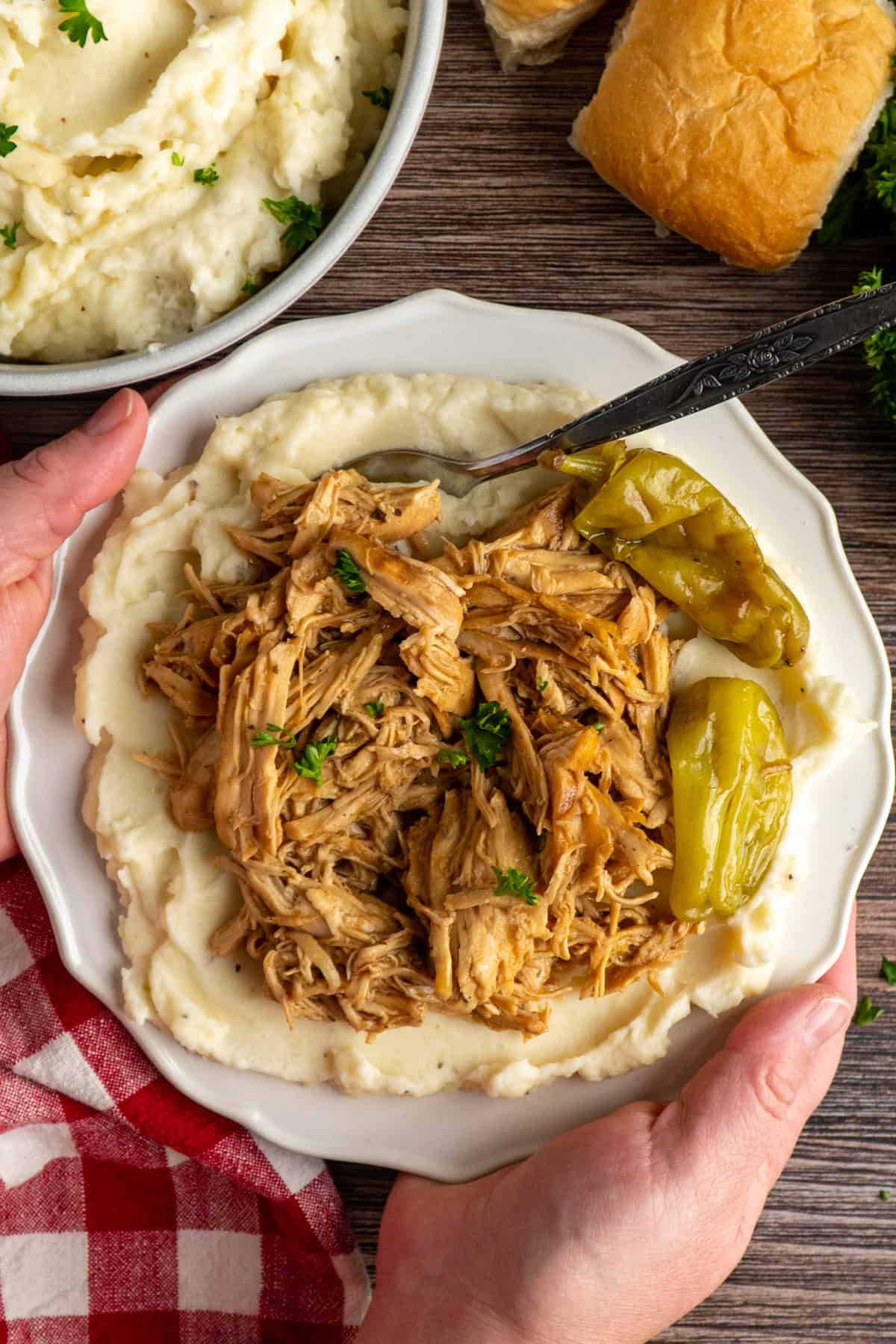 Hands holding a plate with Crock Pot Mississippi chicken on mashed potatoes.