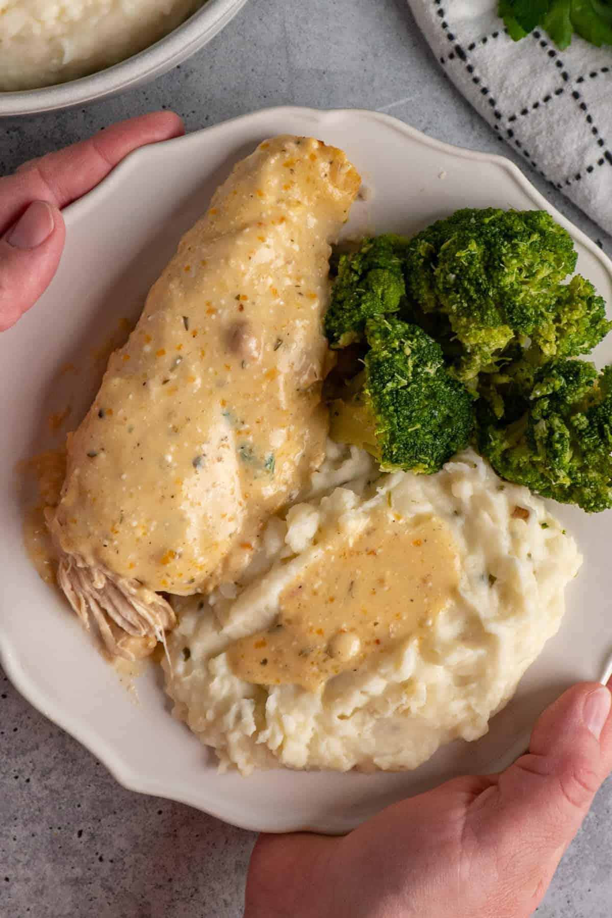 Hands holding a plate of crock pot ranch chicken and mashed potatoes.