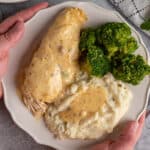 Hands holding a plate of crock pot ranch chicken and mashed potatoes.