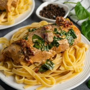 Close up of Crock Pot Tuscan chicken over fettuccine noodles.