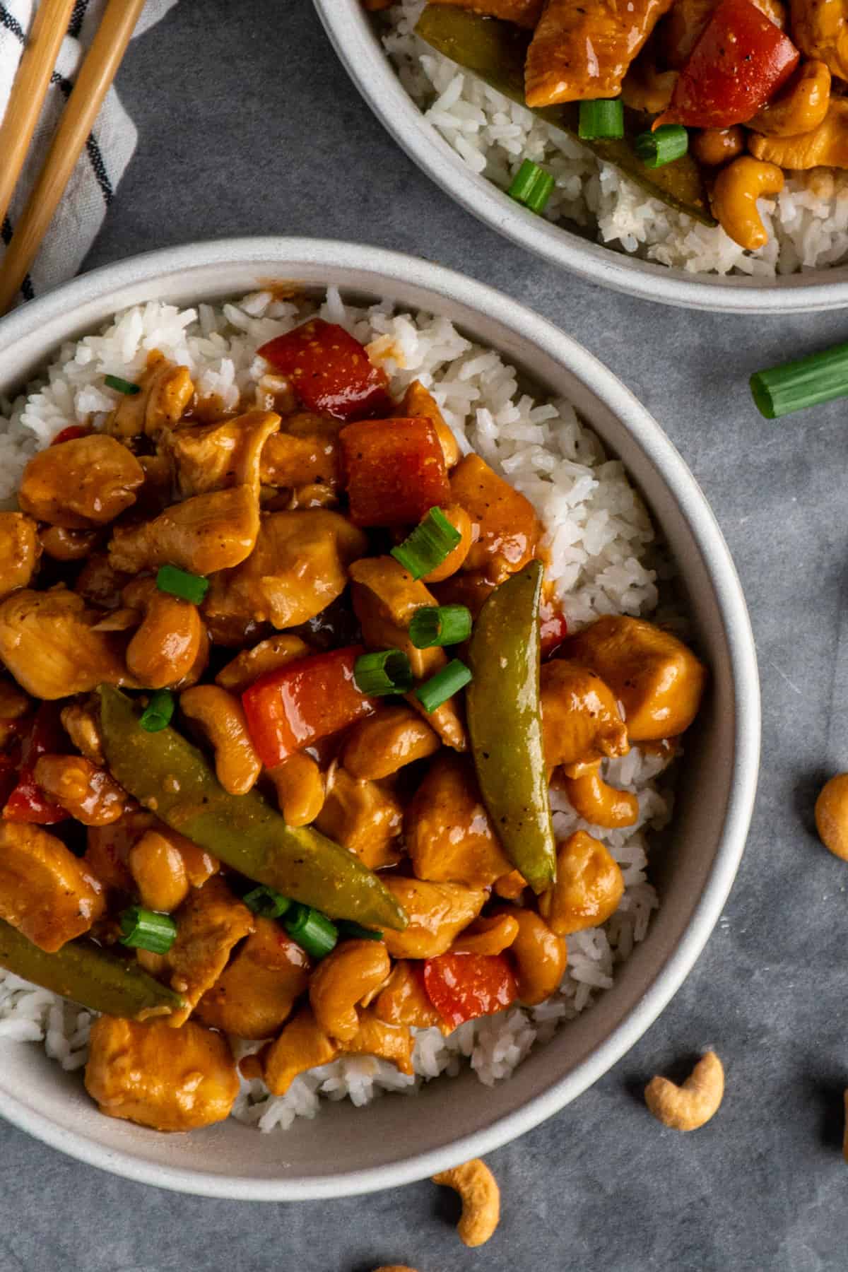 Slow cooker cashew chicken over a bow of rice garnished with green onions.