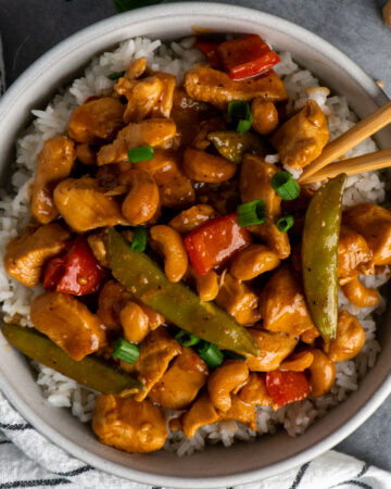 Slow cooker cashew chicken over a bow of rice garnished with green onions.