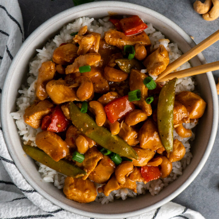 Slow cooker cashew chicken over a bow of rice garnished with green onions.