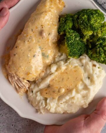 Hands holding a plate of crock pot ranch chicken and mashed potatoes.