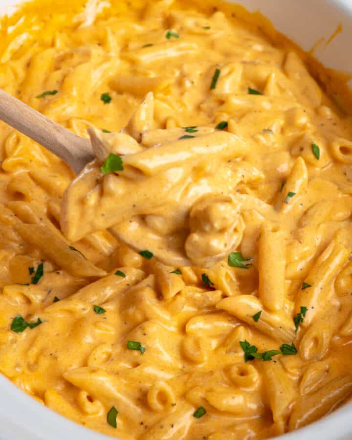 A wooden spoon holding crock pot buffalo chicken pasta.